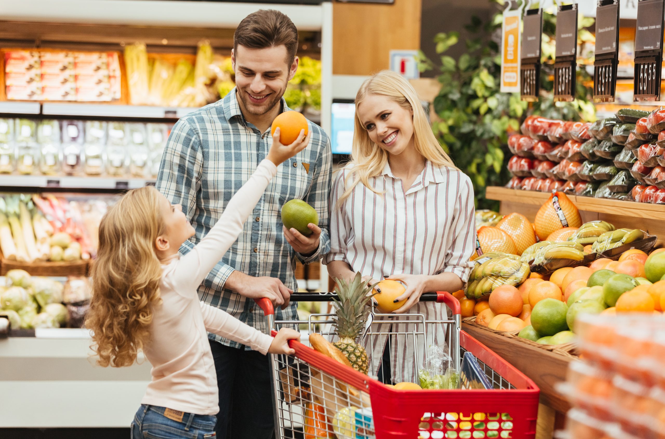 Happy young family standing with a trolley and choosing fruits at the supermarket
